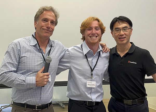 Three men posing together with a microphone and name tag in an indoor setting