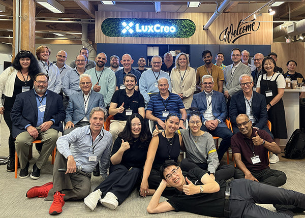 Group of people posing for a photo in an office setting with 'LuxCreo' branding.